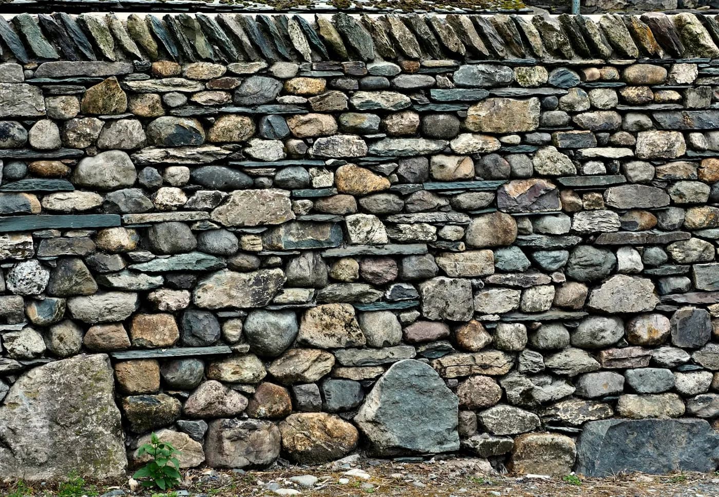 Dry-stone coursework in detail — river rounds pinned with slate, a vertical coping course on top